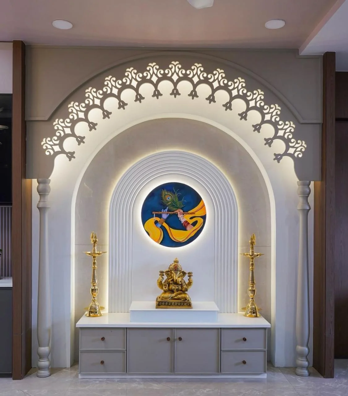 Prayer altar featuring a Ganesha statue, oil lamps, and Krishna painting with ornate fretwork arch.